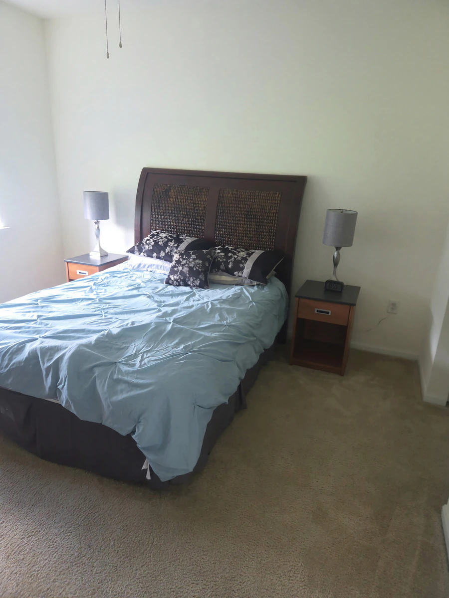 Furnished bedroom with a queen bed, wooden headboard, two nightstands and lamps in a Simpsonville apartment