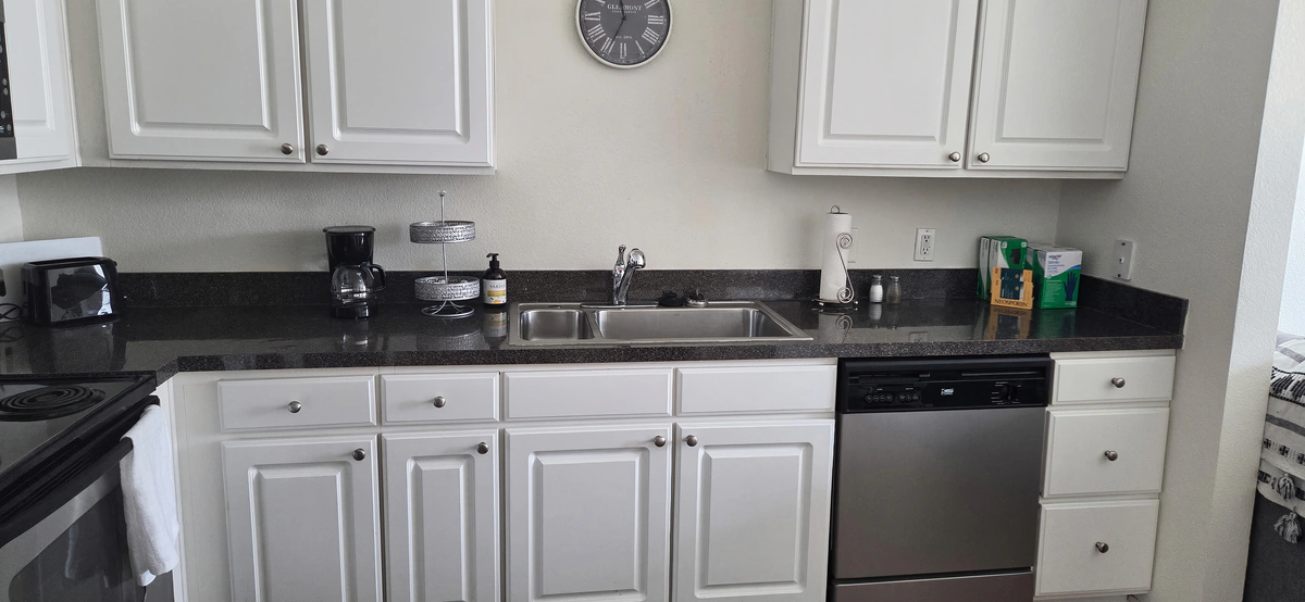 Kitchen with electric range, dishwasher and stocked white cabinets in a furnished Simpsonville apartment